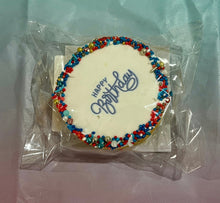 Load image into Gallery viewer, Cookie with 'Happy Birthday' text and colourful sprinkles on a clear plastic bag against a multi coloured background.