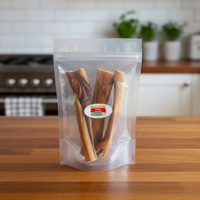Load image into Gallery viewer, A clear plastic stand-up pouch containing several long brown dog treats, with a round white label reading 'Collagen Dog Treats' on the front, photographed against a dark and light kitchen background.