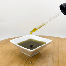 Load image into Gallery viewer, Dropper dispensing hemp seed oil for dogs into a white bowl, showcasing its rich color and texture.