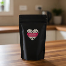 Load image into Gallery viewer, Packaging of banana oat dog cookies in a black pouch with a heart design on a wooden table.