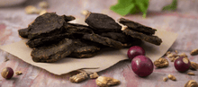 Load image into Gallery viewer, GOURMET DEHYDRATED EMU & BUSH PLUM PATTIES on a paper with fruits and grains beside them.