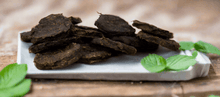 Load image into Gallery viewer, GOURMET DEHYDRATED EMU & RIVER MINT PATTIES 100g on a plate with fresh mint leaves, showcasing a nutritious dog treat.