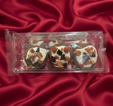 Load image into Gallery viewer, Three chocolate cookies with fruit toppings in a clear plastic packaging on a red satin surface.
