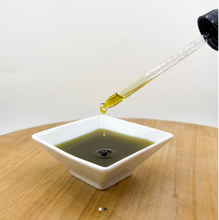 Load image into Gallery viewer, Oil being poured from a dropper into a white square bowl on a wooden surface.
