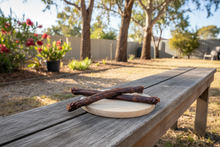 Load image into Gallery viewer, Two dried kangaroo tail sticks on a wooden bench in an Australian back yard
